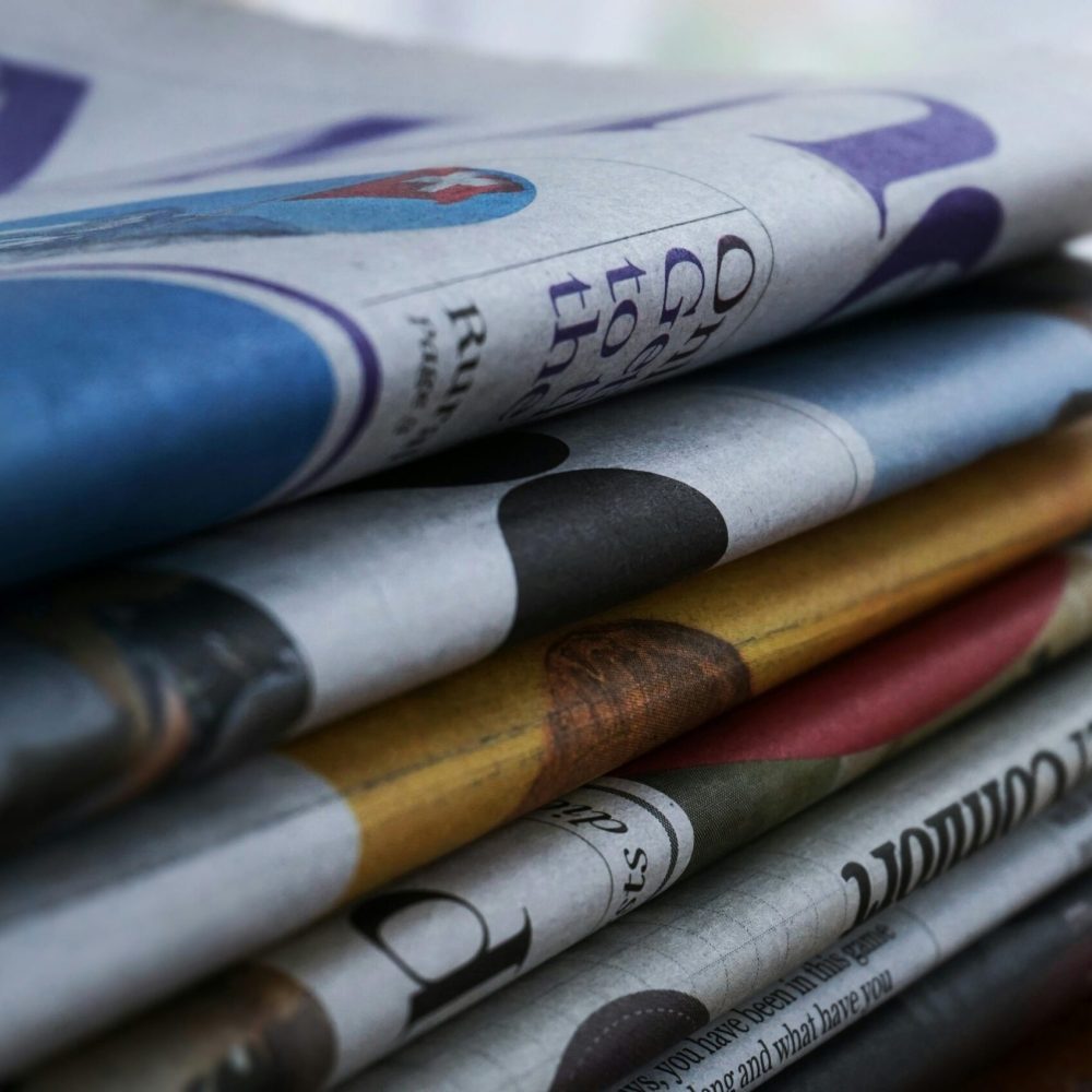 Close-up of a stack of colorful newspapers on a wooden table, showcasing print media.